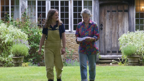 Two gardeners walking across a lawn in front of a house
